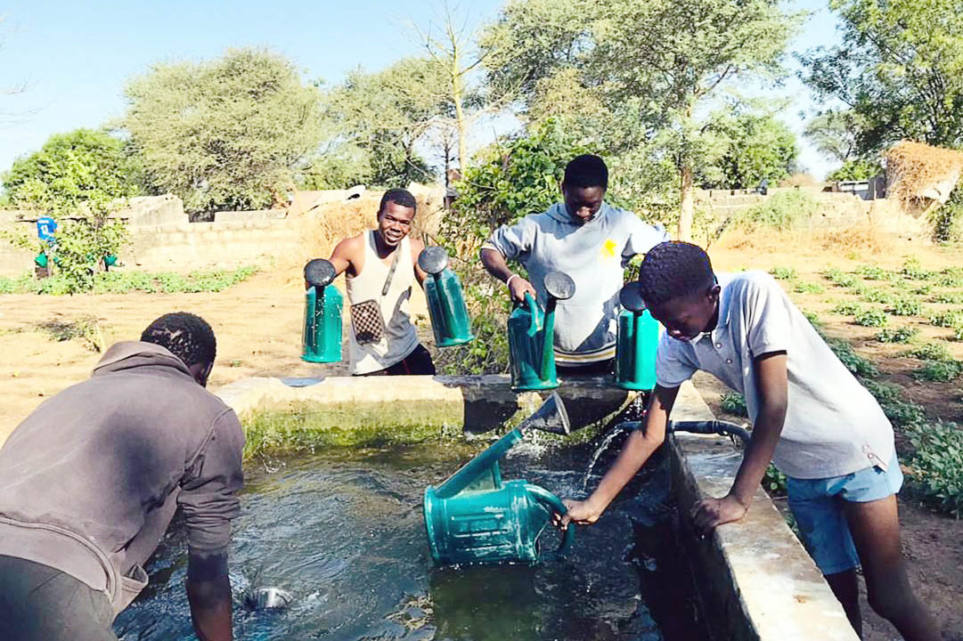 Mehrere junge Männer schöpfen mit Gießkannen Wasser aus einem Brunnen.