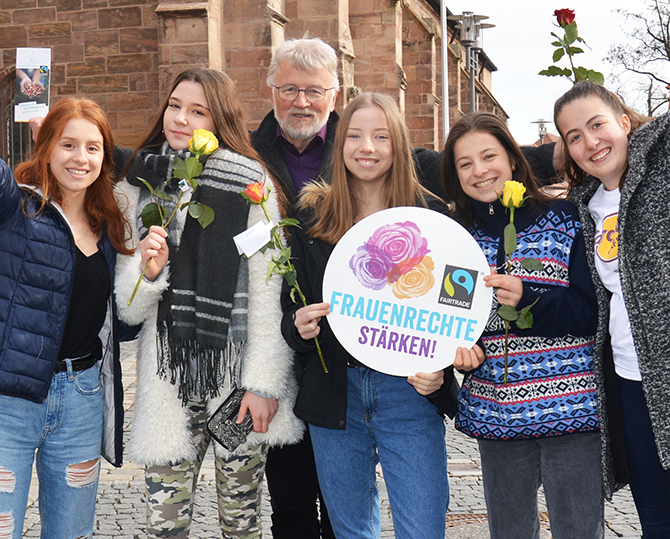Roland Oeser mit einer Gruppe Schülerinnen, die Faire Rosen und Flyer in die Luft halten.