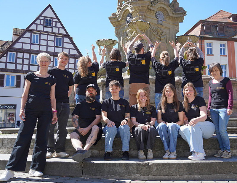 Das Team der Kommunalen Jugendarbeit trägt unisono schwarze Fairtrade-T-Shirts und steht vor dem Schönen Brunnen am Marktplatz.