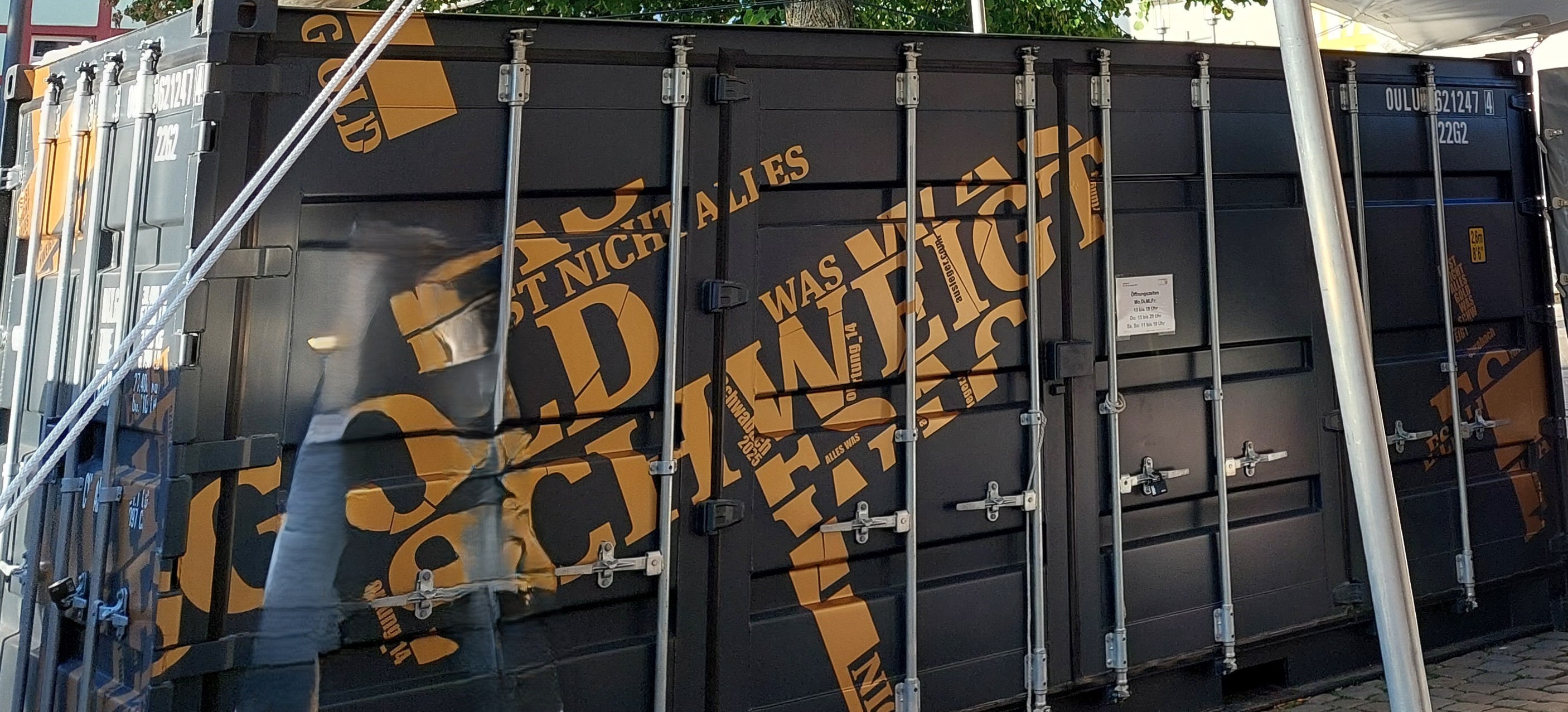 Ein grau-gelb gestalteter Container, auf dem verschiedene Worte zu lesen sind.