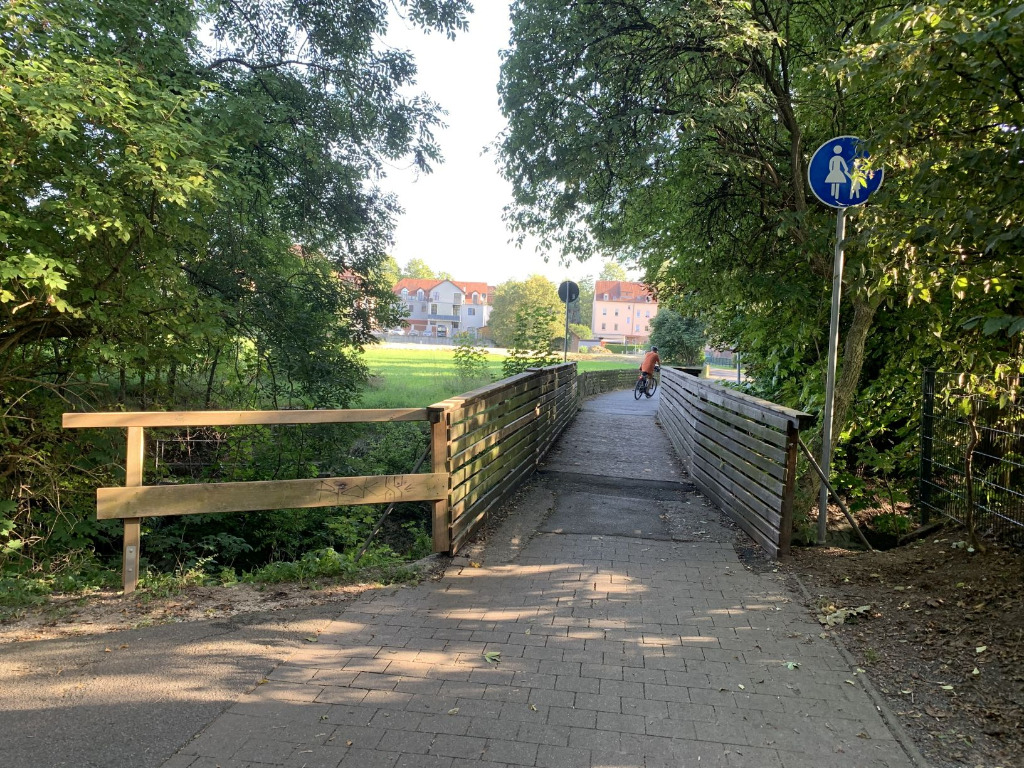 Alte schmale Fußgängerbrücke mit Holzgeländern unter Bäumen